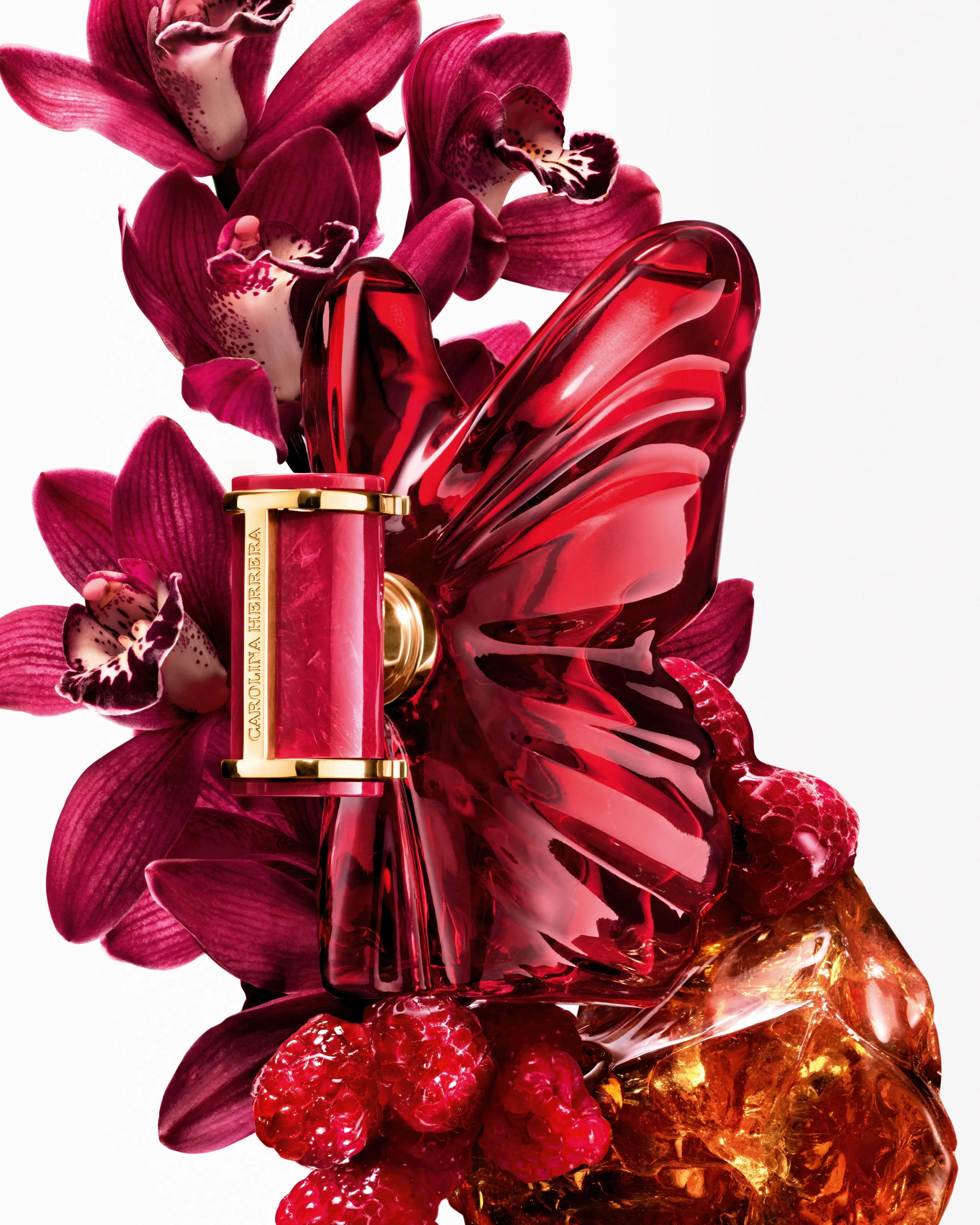 Carolina Herrera "La Bomba" fragrance bottle among red flowers and fruit