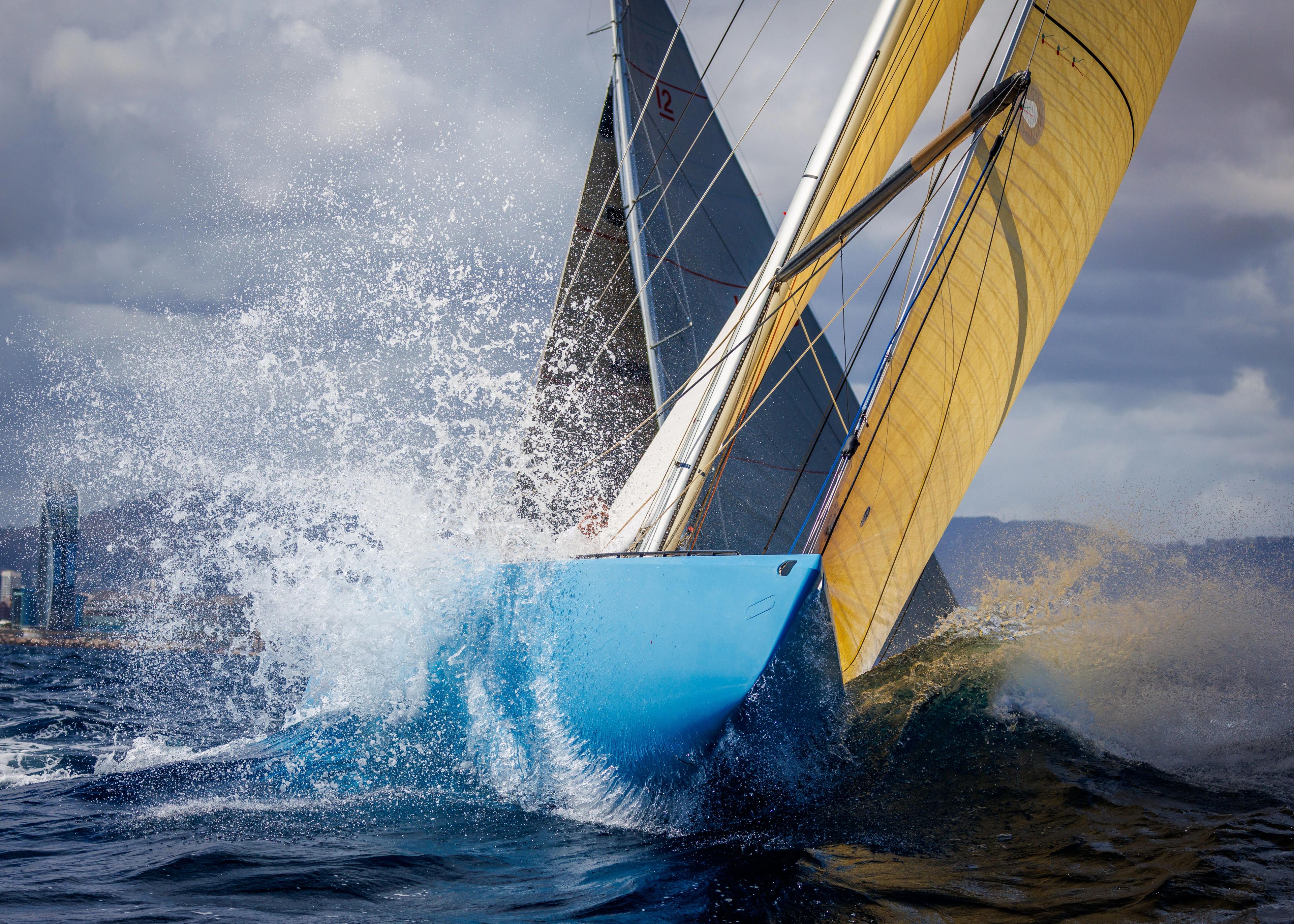 A classic sailing yacht cutting through the water at speed, with waves splashing against its blue hull and yellow sail.