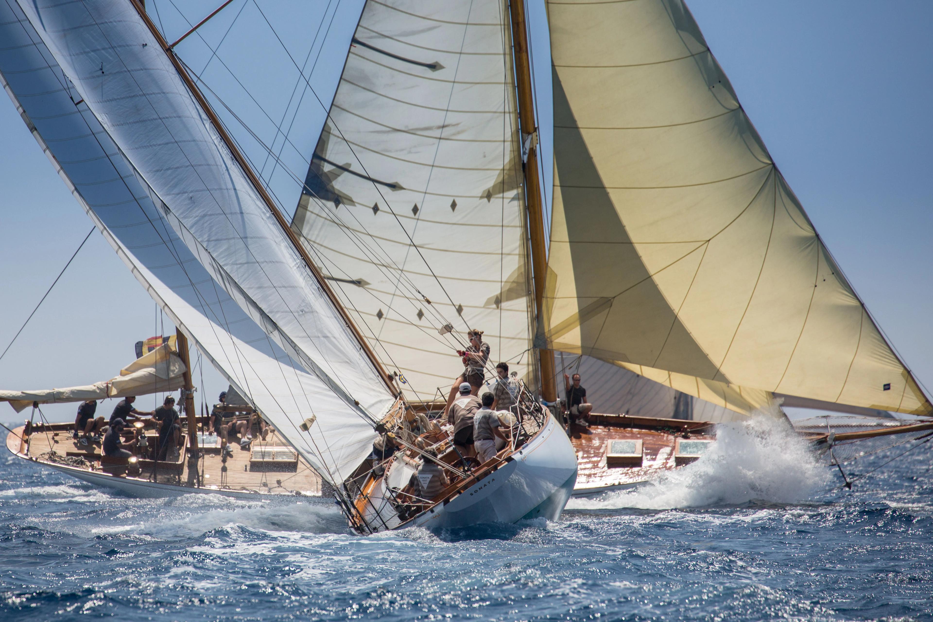 Classic sailing yachts racing at sea during the Puig Vela Clàssica Barcelona regatta, with crews leaning over the deck as the boats cut through the water.