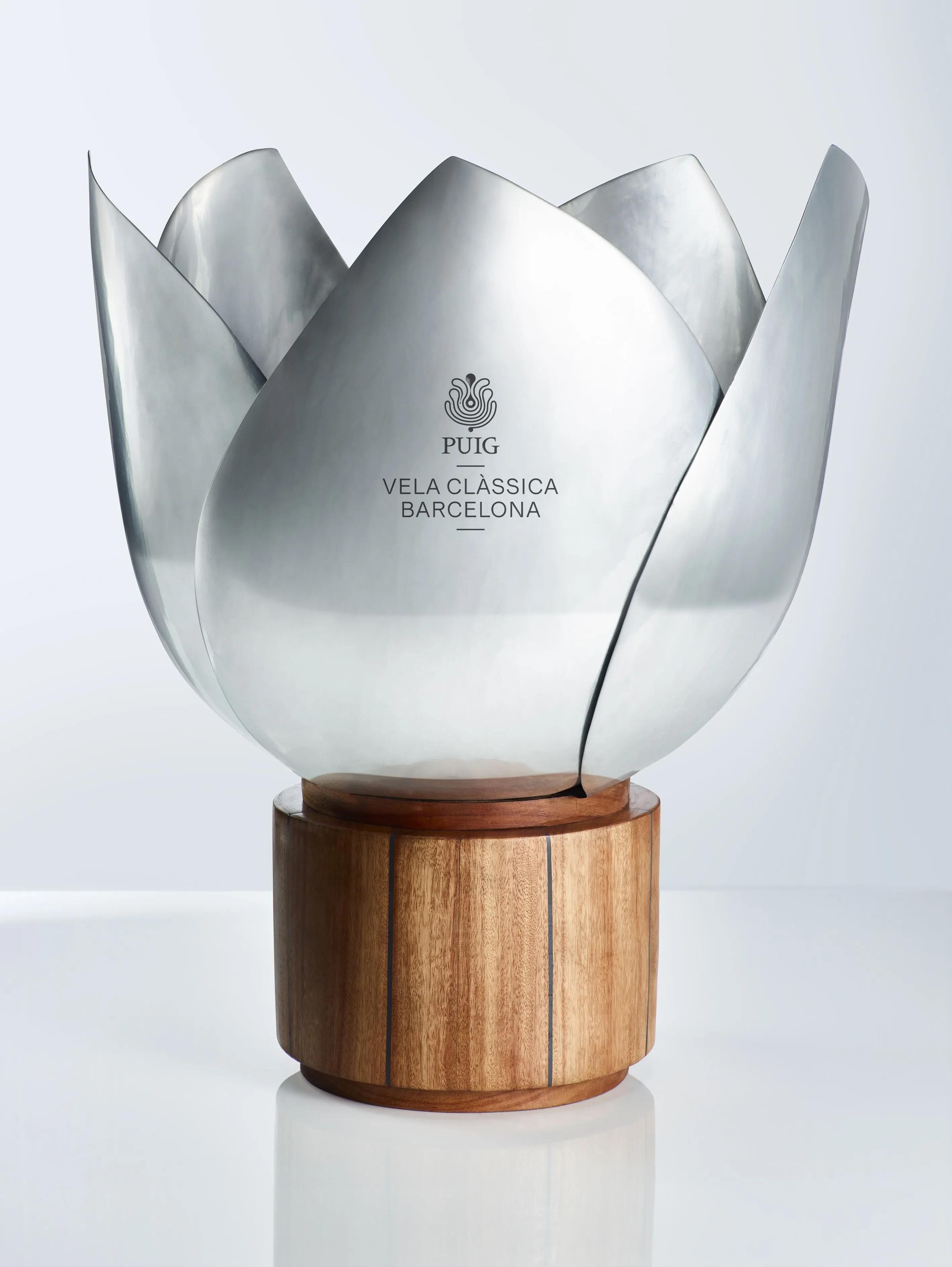 The trophy of the 18th edition of the Puig Vela Clàssica Barcelona, featuring a white sculptural sail-like form on a wooden base.
